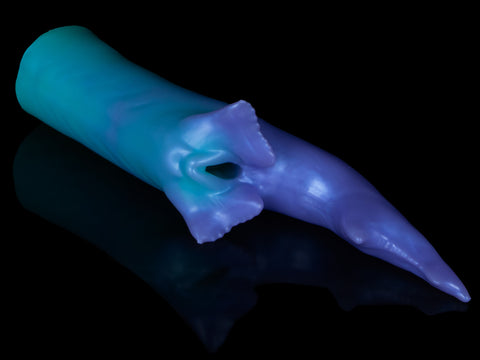 Fantasy shark-inspired silicone stroker in a gradient of teal to purple, featuring subtle ridges, twin pelvic fins framing the entrance, and a long, pointed tail, displayed on a black background.