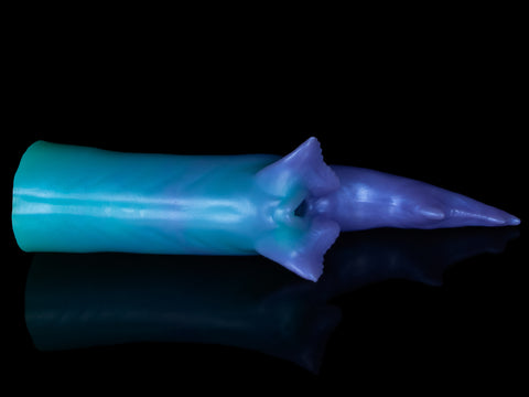 Fantasy shark-inspired silicone stroker in a gradient of teal to purple, featuring subtle ridges, twin pelvic fins framing the entrance, and a long, pointed tail, displayed on a black background.