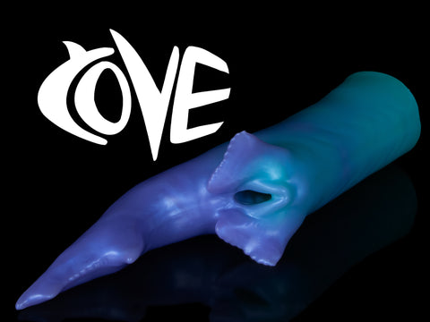 Fantasy shark-inspired silicone stroker titled "COVE" in a gradient of teal to purple, featuring subtle ridges, twin pelvic fins framing the entrance, and a long, pointed tail, displayed on a black background.